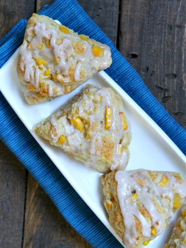 OVERHEAD shot of three fresh peach scones on a white plate with a blue background