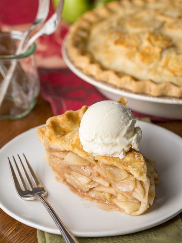 slice of apple pie on a plate with rest of pie in background