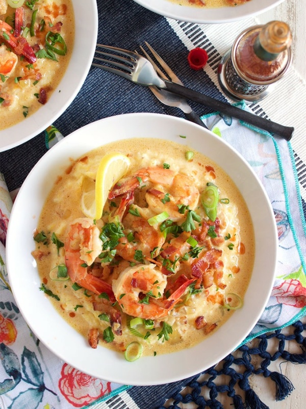 overhead shot of shrimp and grits in a white bowl on a patterned napkin with a fork and two other partial views of shrimp and grits bowls