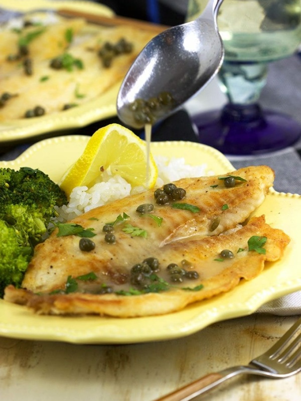 spooning sauce onto plate of tilapia piccata