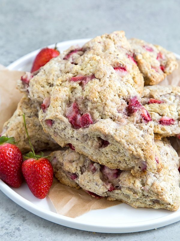 strawberry buttermilk scones stacked on a white plate with a few fresh strawberries