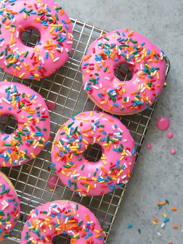 pink glazed doughnuts with rainbow sprinkles on a cooling rack