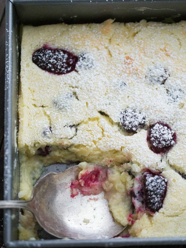 blackberry lemon pudding cake in a metal pan with a serving spoon spooning some of the cake out of the pan