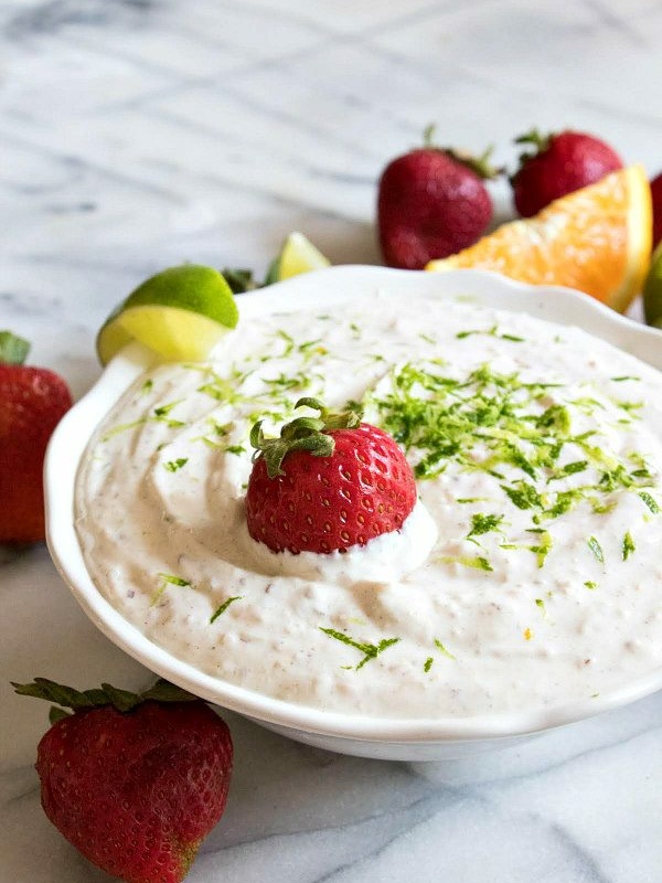 margarita fruit dip garnished with strawberries and lime, displayed in a white bowl on a marble surface