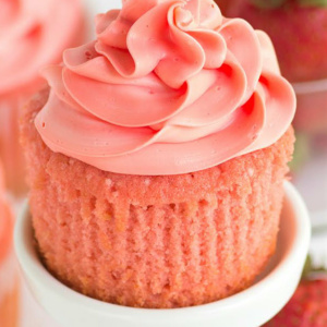 pink strawberry cupcake on a white cupcake stand unwrapped with fresh strawberries on the side