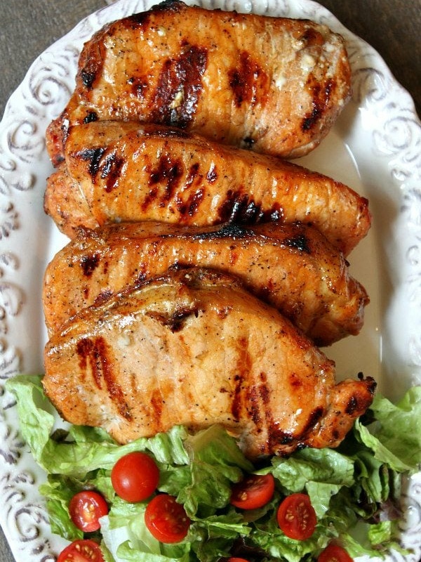 apple and blue cheese stuffed grilled pork chops on a white serving platter with lettuce and tomato salad