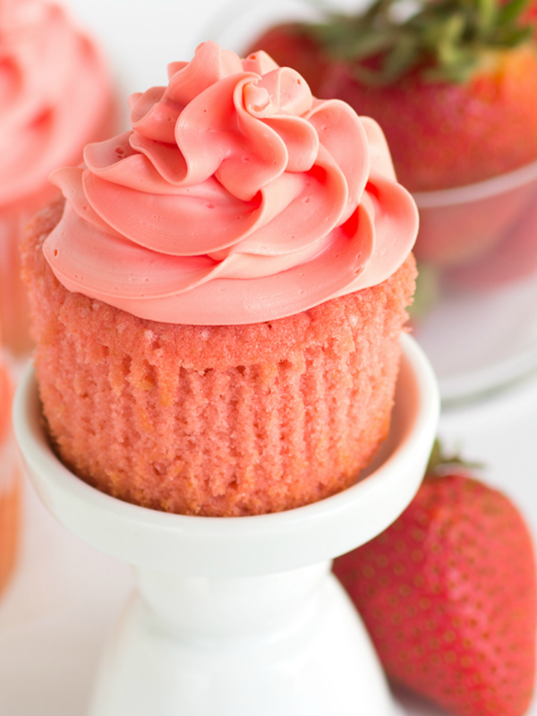 pink strawberry cupcake on a white cupcake stand unwrapped with fresh strawberries on the side