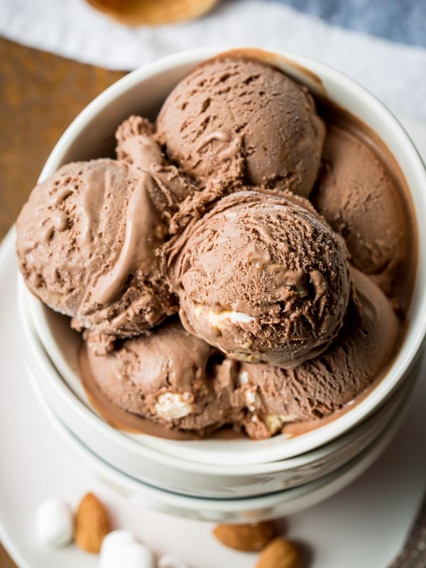 overhead shot of several scoops of rocky road ice cream in a white bowl. marshmallow and almonds scattered in front