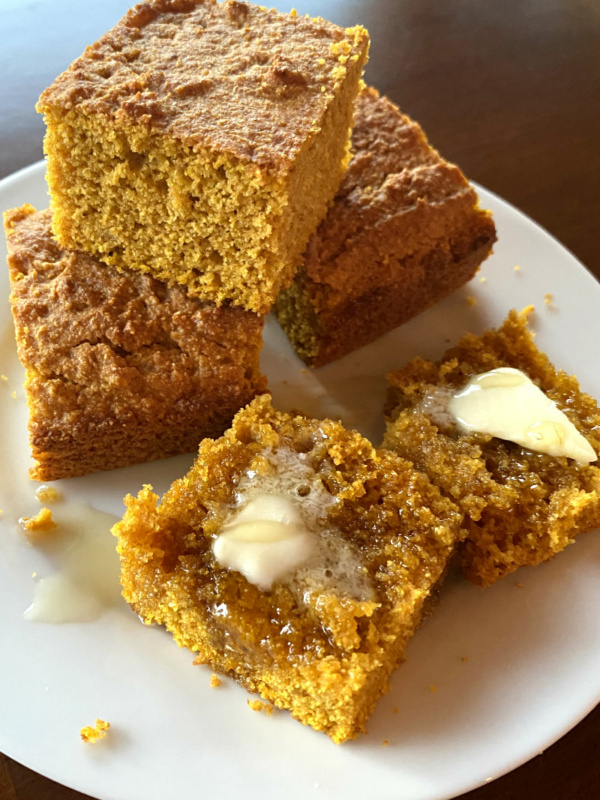 pumpkin cornbread on a white plate sliced with butter