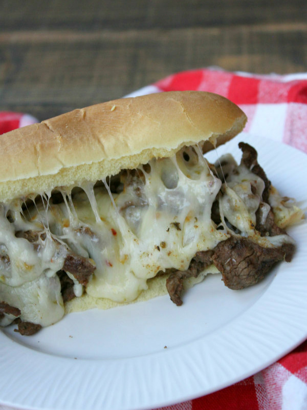 cajun cheesesteak sandwich on a white plate set on a white and red checked napkin