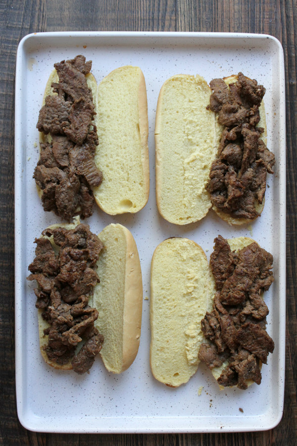 cajun cheesesteak sandwiches open faced on white baking sheet ready to add cheese and bake