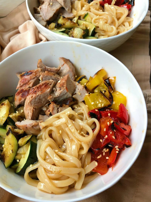 grilled pork and vegetable teriyaki noodle bowl in a white bowl. a peek at a 2nd noodle bowl in the background