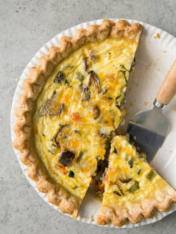 Summer Vegetable Quiche in a white pie plate with a couple of pieces cut out and a pie server on the plate