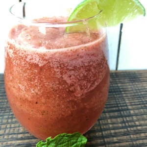 slushie watermelon mojitos in a glass garnished with a lime wedge and a mint leaf in front of the glass