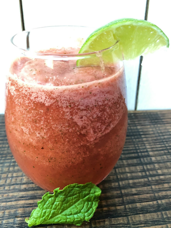 slushie watermelon mojitos in a glass garnished with a lime wedge and a mint leaf in front of the glass