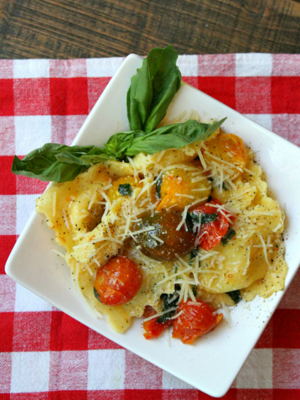 overhead shot of brown butter ravioli with tomatoes on a white plate set on a red/white checked napkin