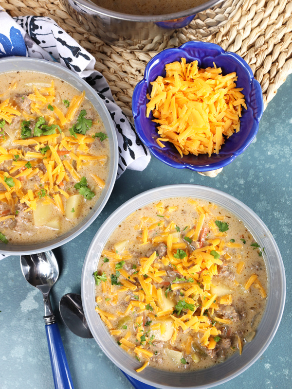 Overhead shot of two bowls of creamy cheeseburger soup with a bowl of grated cheddar cheese.