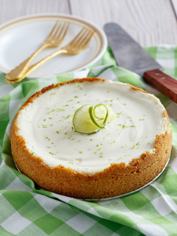 key lime cheesecake set on green/white checked napkin with forks, serving spatula and plates in the background