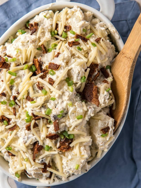 Loaded Baked Potato Salad in a white dish with a wooden spoon on a blue napkin