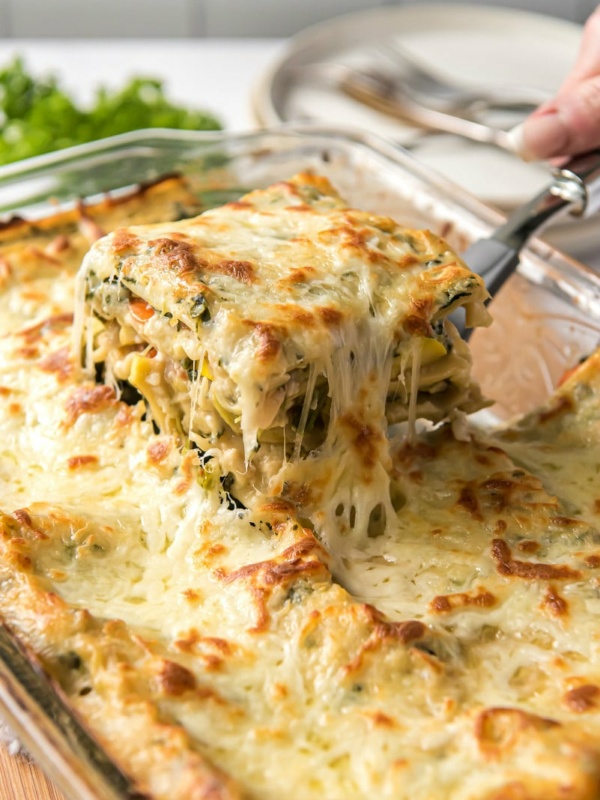 Pulling out a cheesy slice of vegetable lasagna out of the lasagna pan