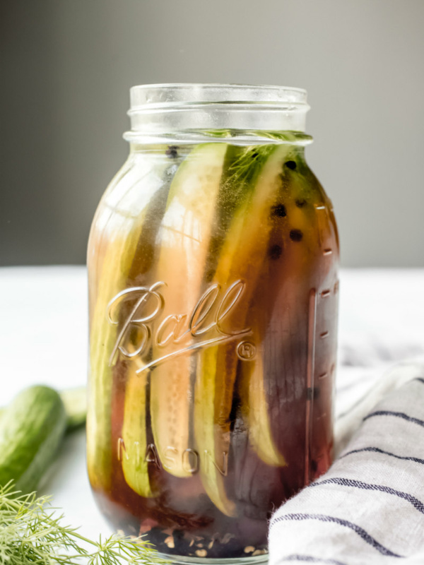 side shot of beer pickles in a tall jar with a blue and white napkin on the side