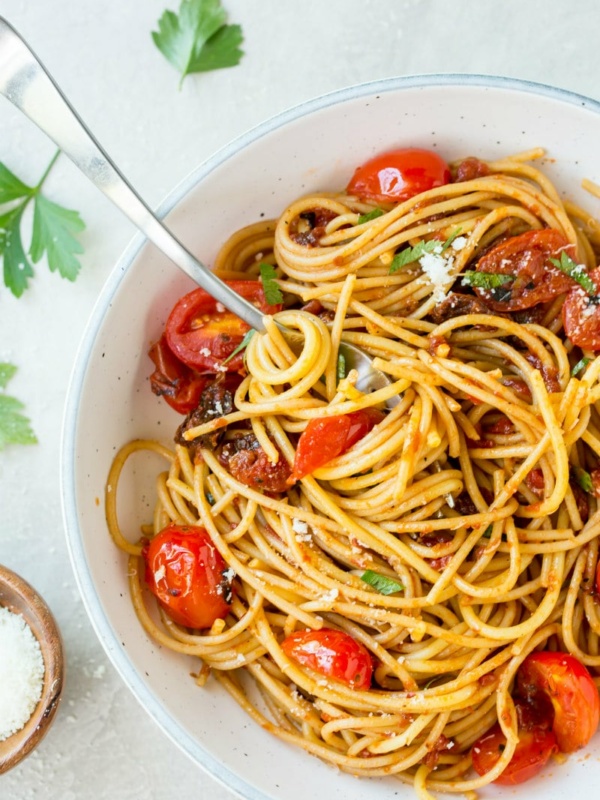 spaghetti with three tomato sauce in a white bowl with a serving spoon