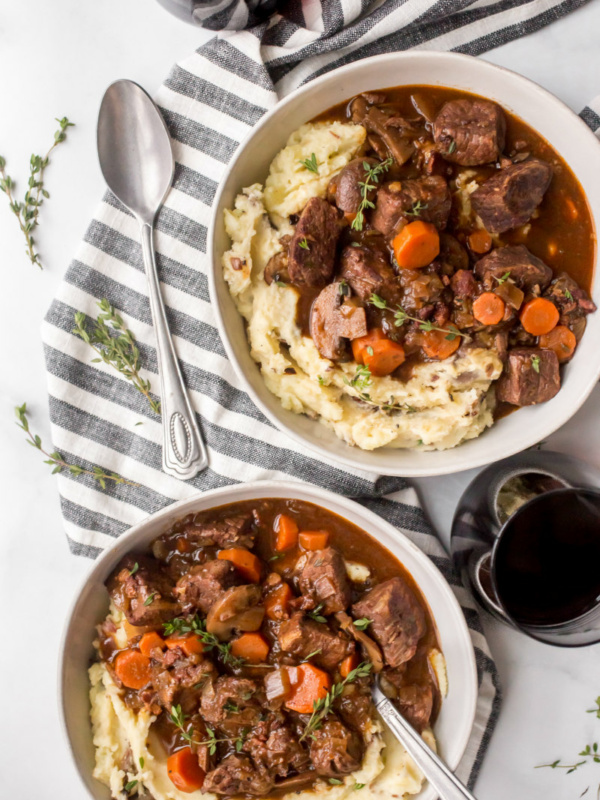 overhead shot of two servings of beef bourguignon displayed on a blue and white striped napkin with a spoon