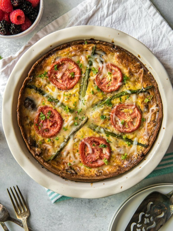 Overhead shot of Garden Vegetable Quiche on a white napkin with forks and fresh fruit in a bowl