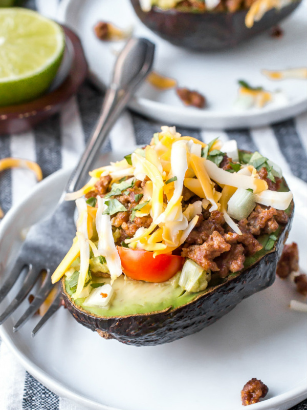 half an avocado stuffed with taco filling. On a white plate with a fork.