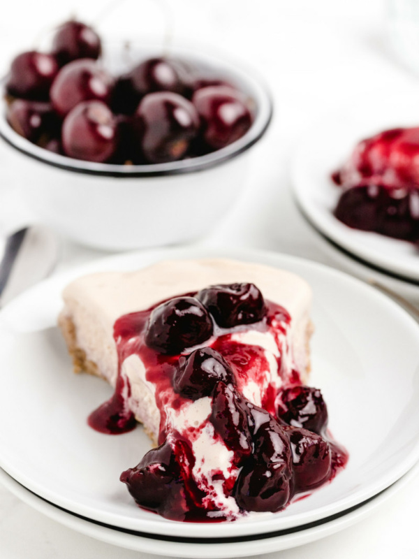 slice of cherries jubilee ice cream pie on a white plate with a bowl of fresh cherries in the background