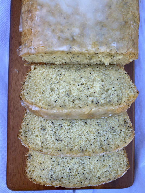 overhead shot of glazed lemon poppy seed bread cut into slices on a wood board