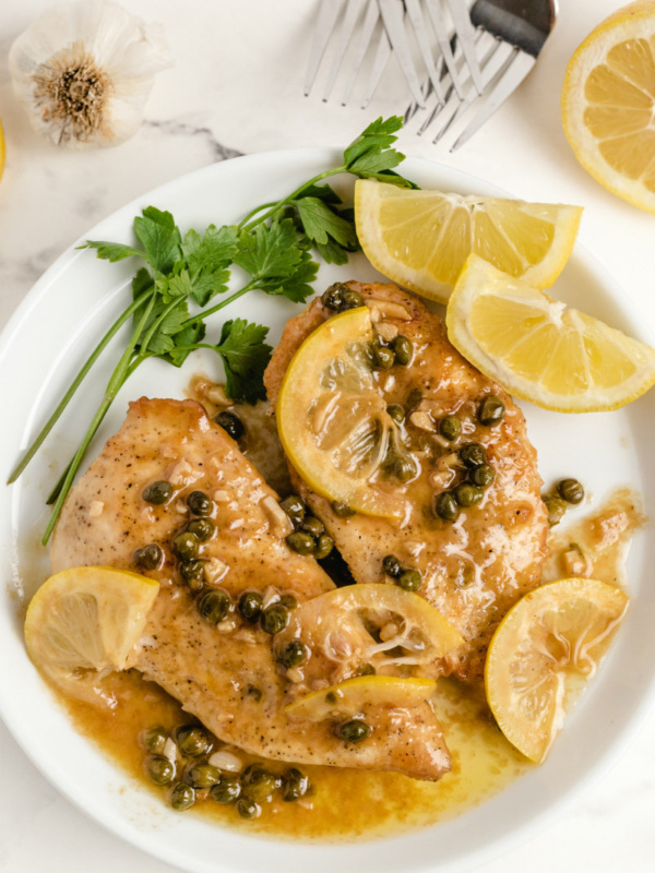 chicken piccata on a white plate with lemon and parsley