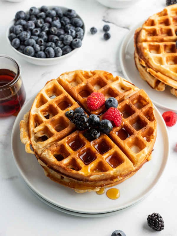 stack of waffles on plate topped with fruit and syrup