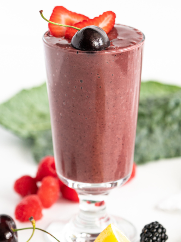 berry detox smoothie in a tall glass with fresh fruit garnishes