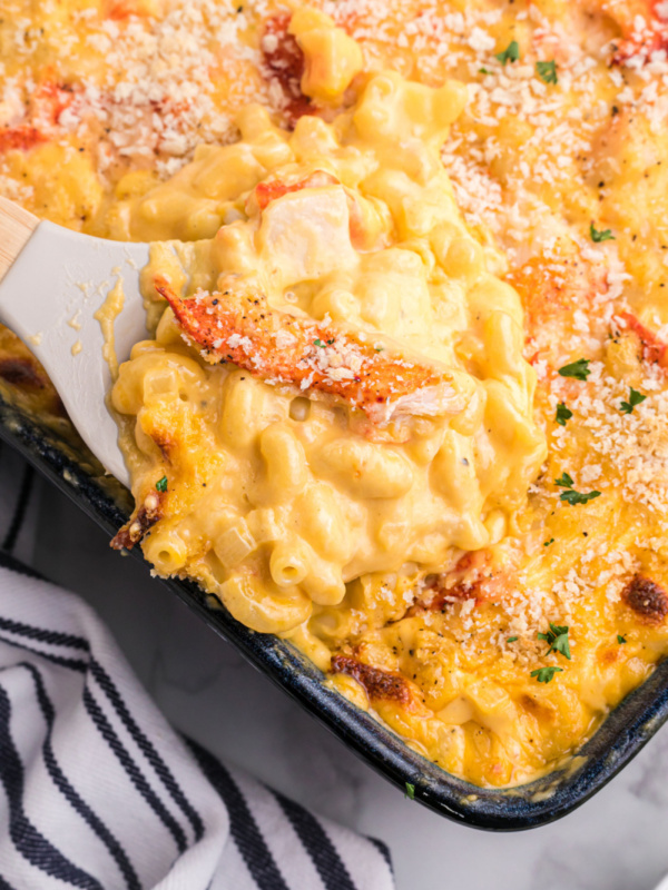 spooning lobster macaroni and cheese out of baking dish