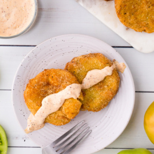 two fried green tomatoes on a plate topped with remoulade sauce