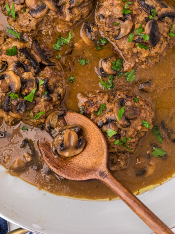 salisbury steak in a skillet with a wooden spoon