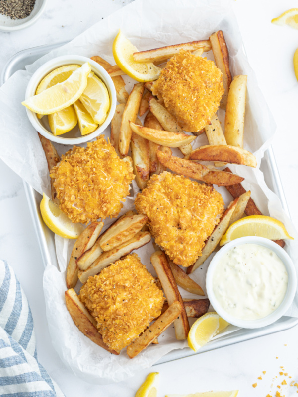 baked fish and chips in pan with lemon wedges and sauce