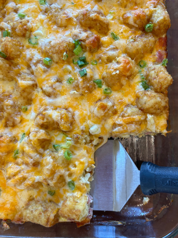 tater tot breakfast casserole in dish with spatula taking out serving