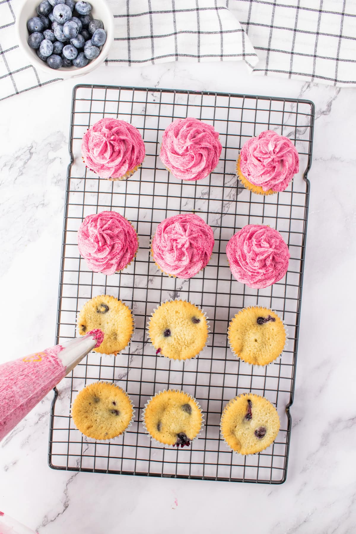 blueberry cupcakes on a rack being frosted