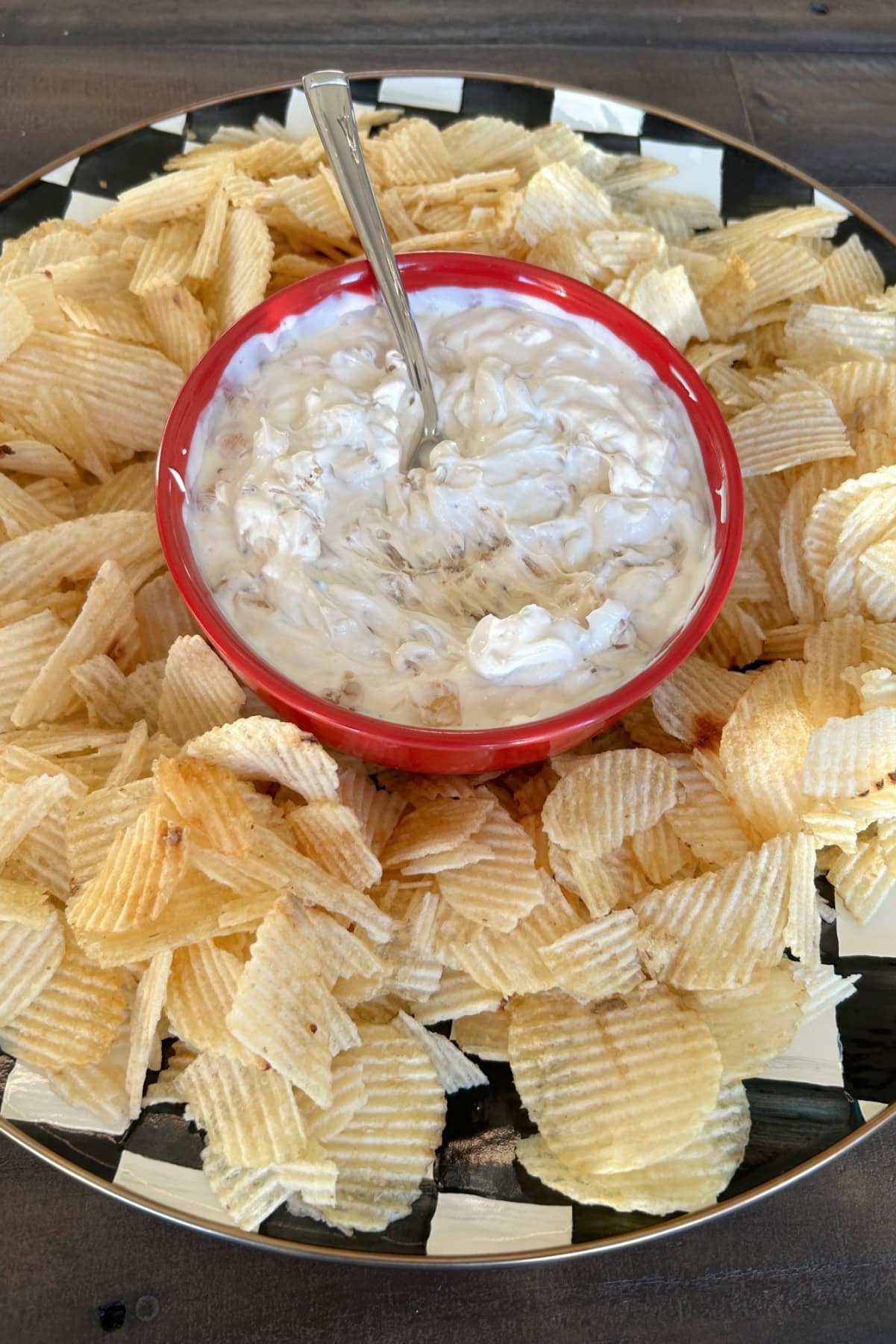red bowl of caramelized onion dip on platter with potato chips