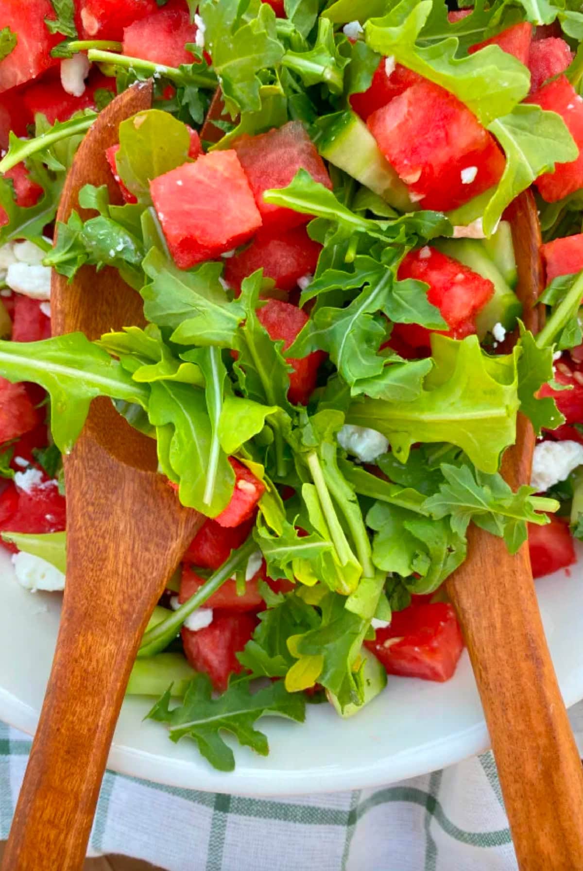 watermelon cucumber and feta arugula salad in bowl with tongs