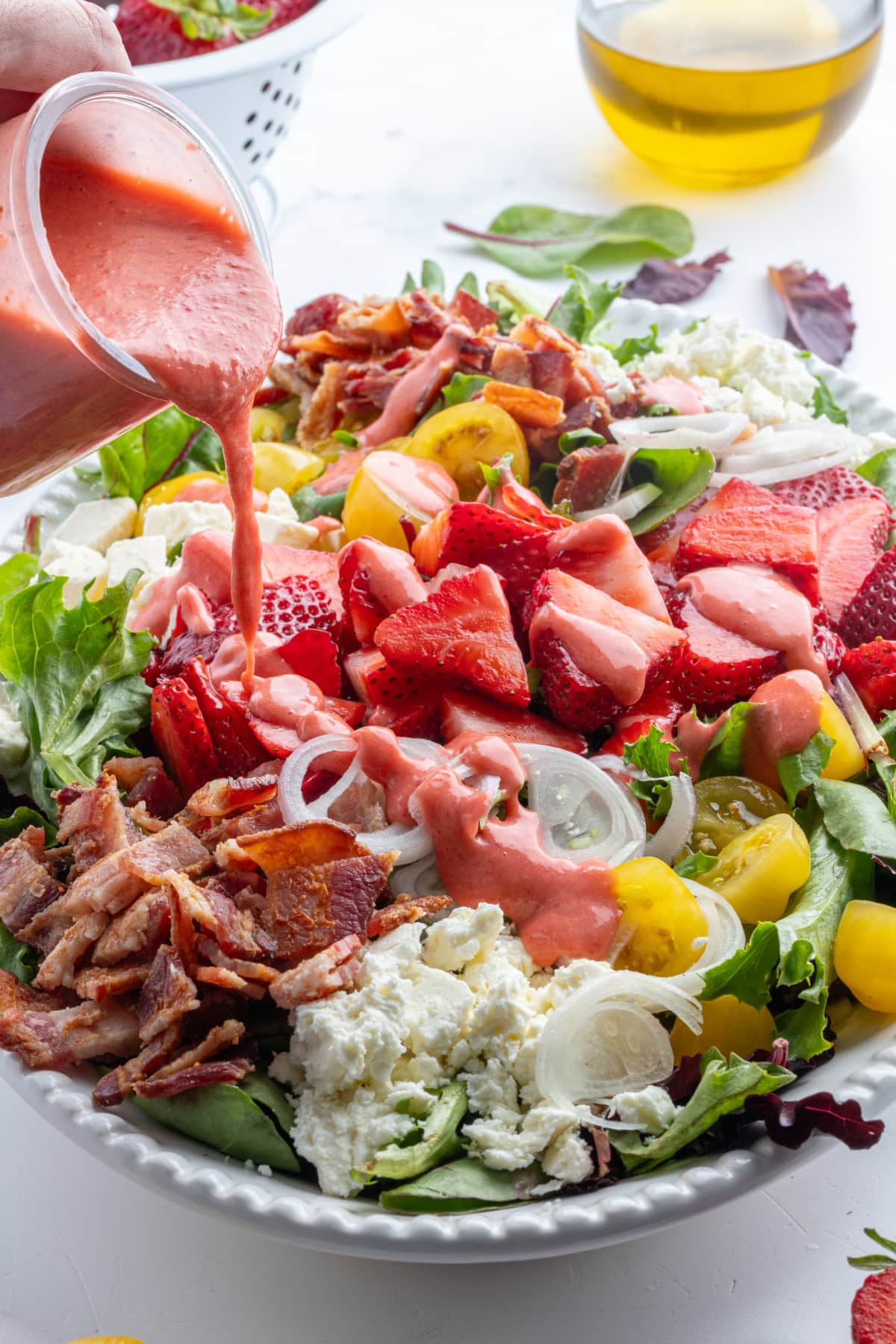 pouring strawberry vinaigrette onto berry bacon and tomato salad