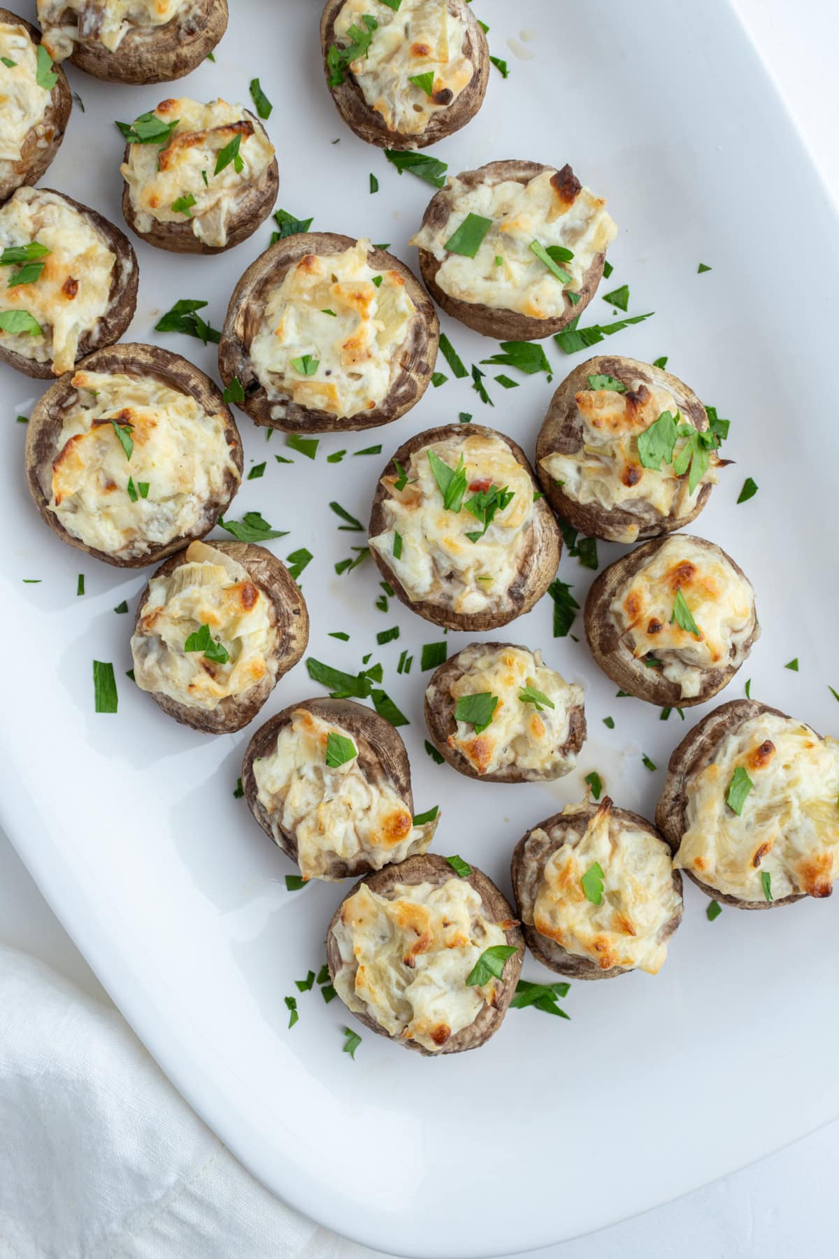 overhead shot of artichoke stuffed mushrooms on white platter