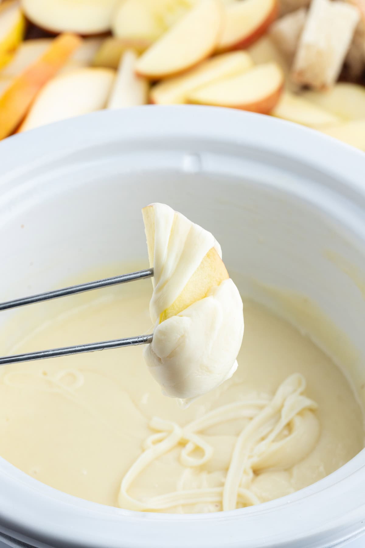 fork holding apple slice that has just been dunked into swiss cheese fondue